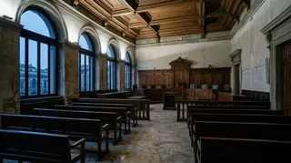 Fondo sentenze della manovra: un'aula di tribunale italiana deserta all'alba, con i banchi vuoti e il seggio del collegio