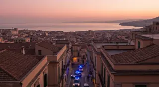 Blitz Ndrangheta Reggio Calabria: auto della polizia con lampeggianti blu all'alba tra i tetti della citta sullo Stretto