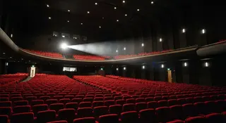 Odissea al box office: sala cinematografica gremita di poltrone rosse illuminate dal proiettore
