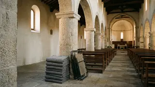 Rimozione di don Biancalani: navata di una chiesa parrocchiale vuota con coperte piegate e brandine richiuse nella navata laterale
