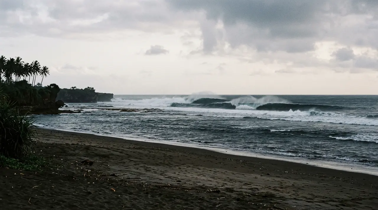 Gabriele Bellucci è morto surfando a Bali: le onde frangono su un reef dell'oceano Indiano davanti a una spiaggia di sabbia scura deserta all'alba