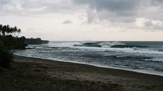Gabriele Bellucci è morto surfando a Bali: le onde frangono su un reef dell'oceano Indiano davanti a una spiaggia di sabbia scura deserta all'alba