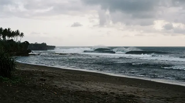 Gabriele Bellucci è morto surfando a Bali: le onde frangono su un reef dell'oceano Indiano davanti a una spiaggia di sabbia scura deserta all'alba