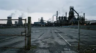 Lettere di licenziamento nell'indotto ex Ilva: lo stabilimento siderurgico di Taranto visto da un cancello chiuso all'alba